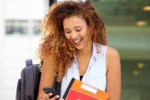 Close up happy female student with curly hair looking at cellphone